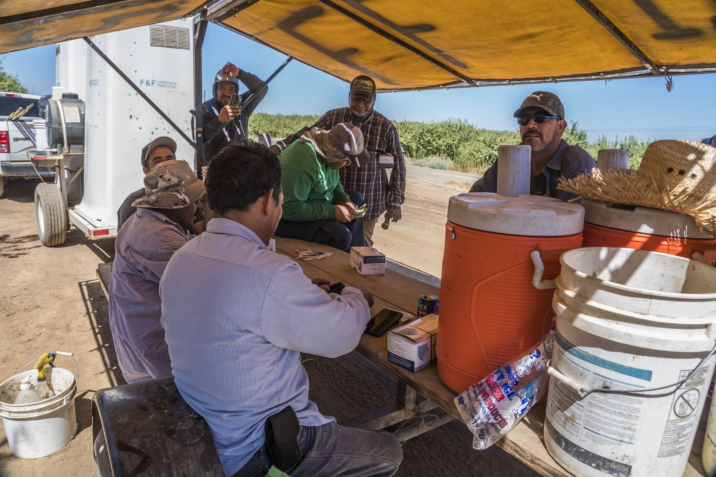 Farmworkers rest and drink water in shaded area